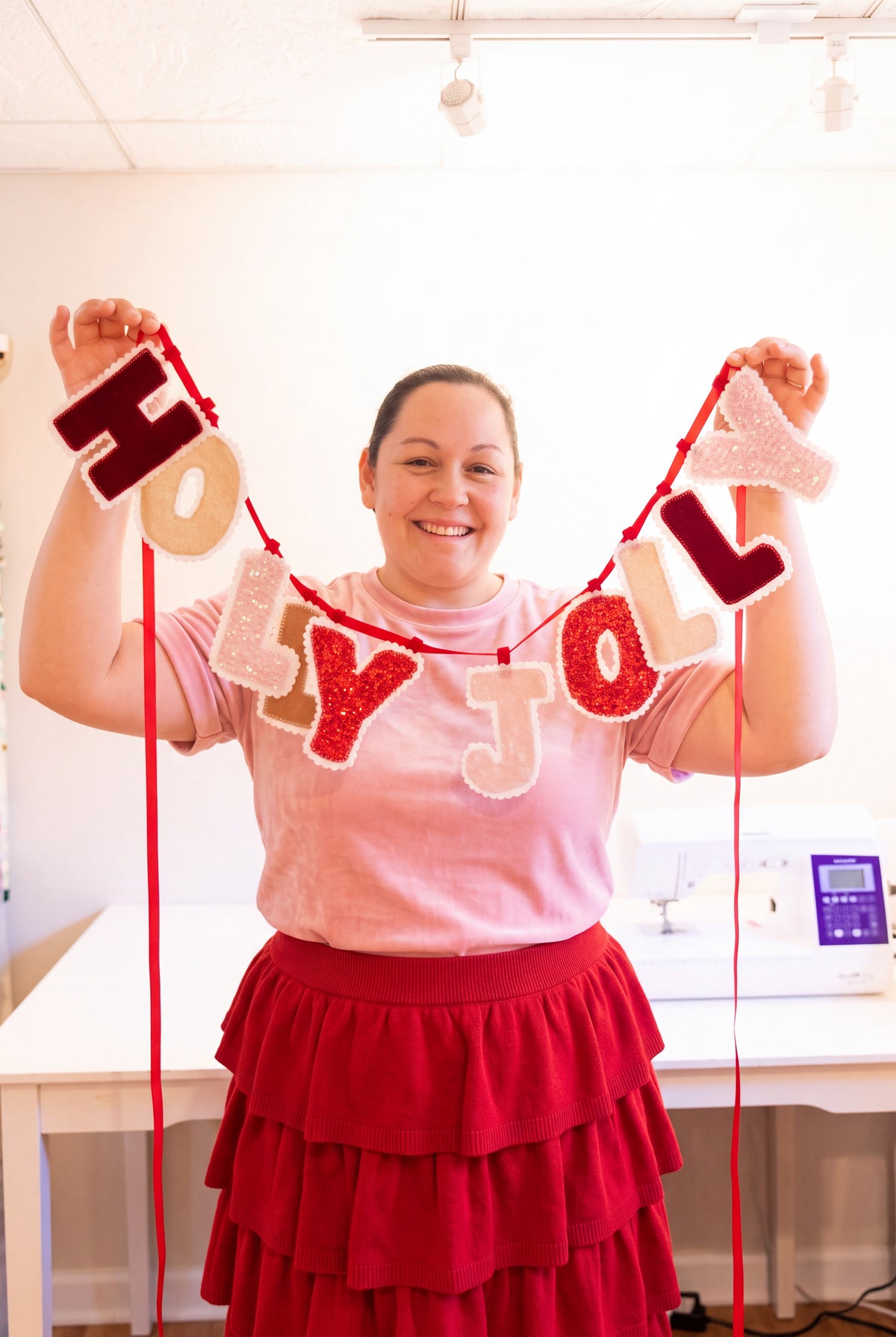 Handmade HOLLY JOLLY Christmas fabric banner featuring pink and red velvet and sequin letters with white scalloped edges, hanging from a red ribbon.